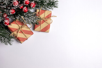 Two craft packed christmas presents wrapped in striped red and kraft paper with a branch of green spruce fur tree with snow and holly on white background top view copy space.