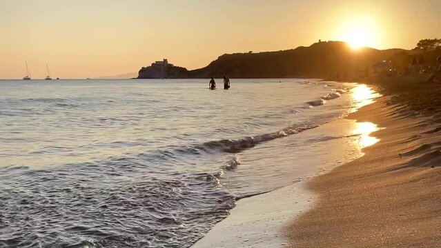 Beach waves at sunset time with setting sun, beautiful waves rolling in to the sandy beach, colorful sunlight reflecting on water surface