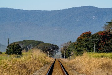 Scenic shot of an empty train track in a rural area with high mountains in the background