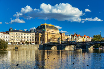 National Theatre located in Prague, Czech Republic on the Vltava River. Legion bridge on river Vltava. National Theatre (Narodni Divadlo) on embankment in sunbeams of evening sunset sunlight. Prague