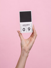 Female hand holding wooden calendar with date January 09 on pink background