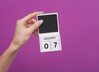 Female hand holding wooden calendar with date January 07 on purple background