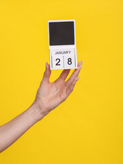 Female hand holding wooden calendar with date January 28 on yellow background