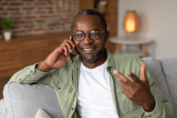 Portrait of cheerful middle aged african american male in glasses calls by smartphone,...