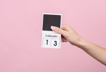 Female hand holding wooden calendar with date February 13 on pink background