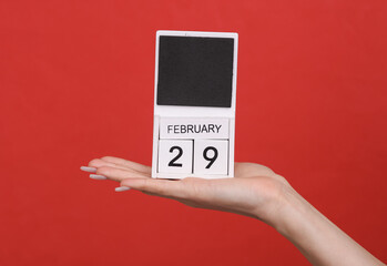 Female hand holding wooden calendar with date February 29 on red background