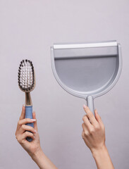 Woman's hand holding a cleaning brush and a dustpan on a gray background