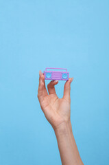 Female hand holding a miniature of retro boombox tape recorder on blue background.