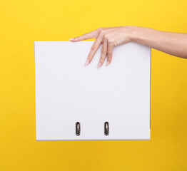 Woman's hand holds white binder with rings on a yellow background