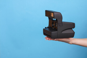 Female hand holding instant retro camera on blue background