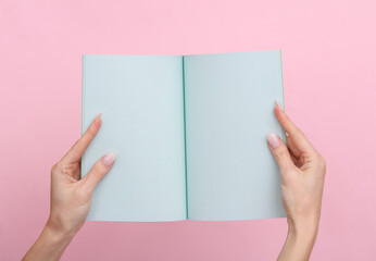 Obraz premium Female hands hold a notepad with blue sheets of paper on a pink pastel background.