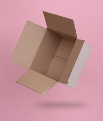 Empty open cardboard box levitating on pink background with shadow