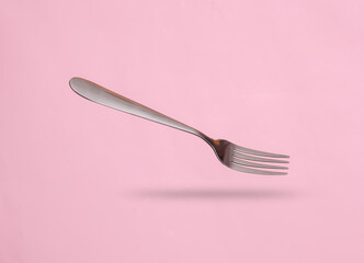 Metal fork levitating on pink background with shadow