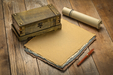 sheets and roll of blank handmade paper with rough edges and a retro storage box against rustic...
