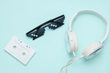 Stereo headphones with Pixelated 8 bit sunglasses and audio cassette on blue pastel background