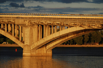 Fototapeta na wymiar Reinforced concrete bridge support. Arch and elements of the arch structure. Sunset of the day.