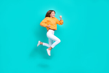 Fototapeta na wymiar Full length photo of cheerful hurrying school girl dressed orange hoodie jumping high running fast isolated teal color background