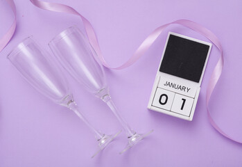 New Year celebration. Glasses and calendar with the date January 01, satin ribbon on a lavender...