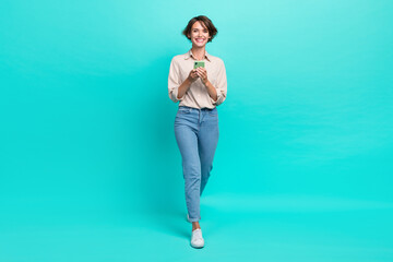 Full length photo of cheerful lady walk outside use gadget gps navigation map go city center meeting friends isolated cyan color background