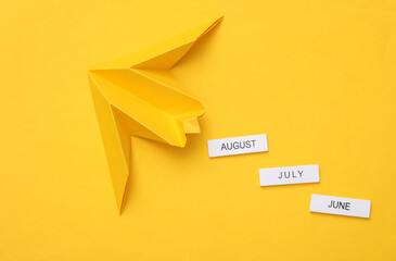 The transience of time. Origami airplane with summer months on yellow background