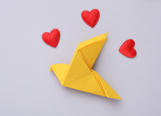 Yellow origami dove with hearts on a gray background. Peace symbol, no war