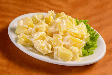 Potato salad mayonnaise in white bowl on wooden background.