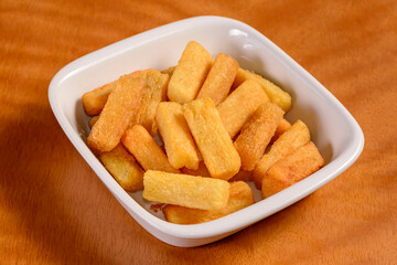 Fried cassava. Small portion of chips in white bowl on wooden background.