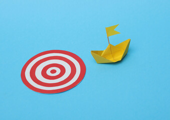 Leadership, pursuit of goals, business concept. Paper boat and a target on a blue background