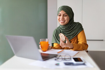 Young Muslim Woman Eating Snacks In Front Of Laptop At Home