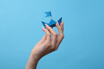 Fototapeta na wymiar Hand holding blue paper boat on blue background