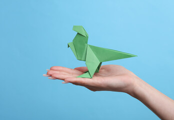 Female hand holds origami dinosaur on blue background. Hobby, creativity