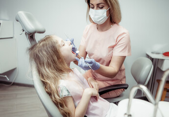 Sweet little girl in the dental chair. The dentist examines the teeth of the child's patient....