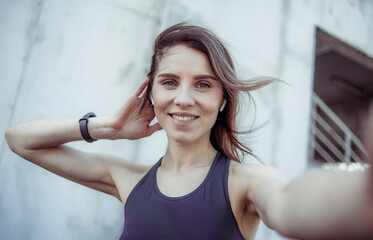 Selfie portrait of a beautiful fitness woman in headphones in an urban location