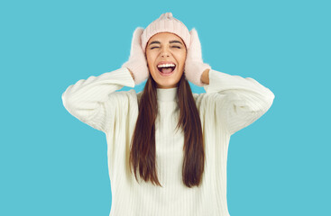 Portrait of young woman frantically reacting to huge winter sales and crazy holiday discounts. Caucasian woman in mittens and hat grabs head and screams excitedly isolated on light blue background.