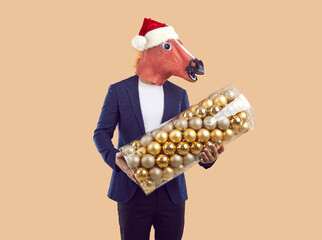 Studio shot of man wearing funny costume holding Christmas tree balls. Man in suit, Santa cap and...