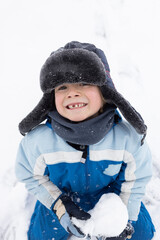 portrait of a preschooler boy in a warm fur hat with a snowball in hands in cold winter season. Active lifestyle, joy every day. Toothless joyful smile of child. happy childhood. Frosty weather