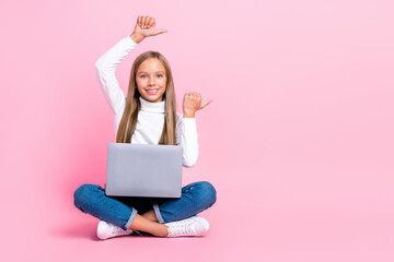 Obraz na płótnie Canvas Full body portrait of cheerful girl sit floor use netbook indicate thumb fingers empty space isolated on pink color background