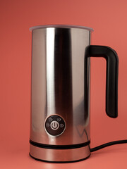 Automatic milk foam maker. Stainless steel milk frother with buttons and power cord on a pink background.