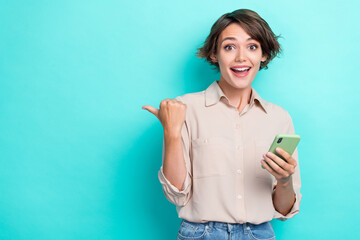 Portrait of impressed ecstatic girl with brunette hair beige shirt hold phone directing empty space...