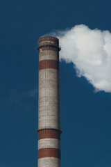 Pollution of the environment, ecology and air. Withdrawal of combustion products of soot, smoke and gases from the pipe of an industrial plant into the atmosphere against the background of a blue sky