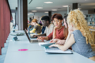 Group of students from different cultures and backgrounds studying together in the library