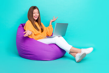 Full length photo of pretty funky school girl dressed orange hoodie bean bag talking device empty space isolated teal color background