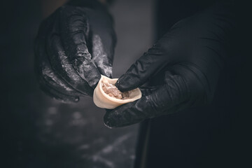 Hands in black gloves sculpt dumplings close-up, with shallow depth of field