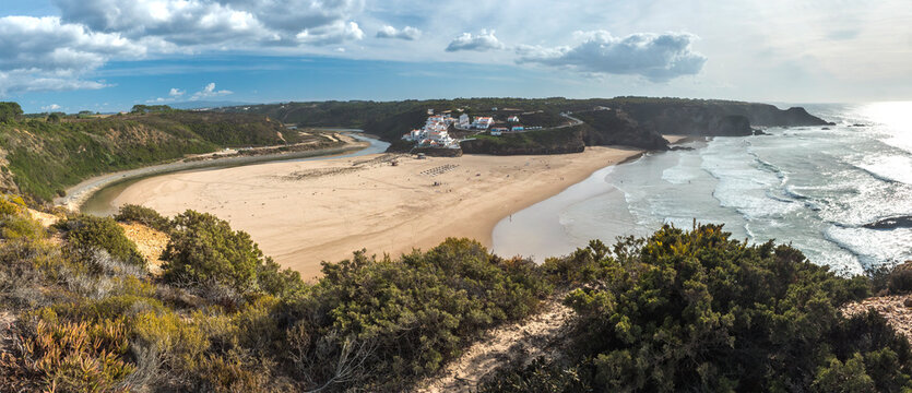 Panoramic view of Praia de Odeceixe Mar Surfer beach with golden sand, atlantic ocean waves, river bend and white houses of Odeceixe village. Rota Vicentina coast, Odemira, Portugal.