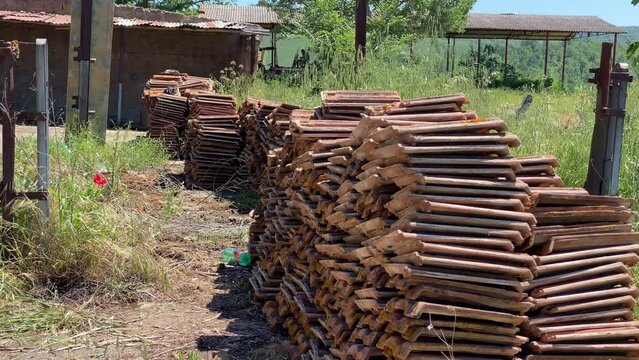 Heap of unnecessary dismantled roof tiles on construction side, mossed red clay roof tiles demolished from old house unusable for new construction or renovation. Terracotta tiles garbage near the