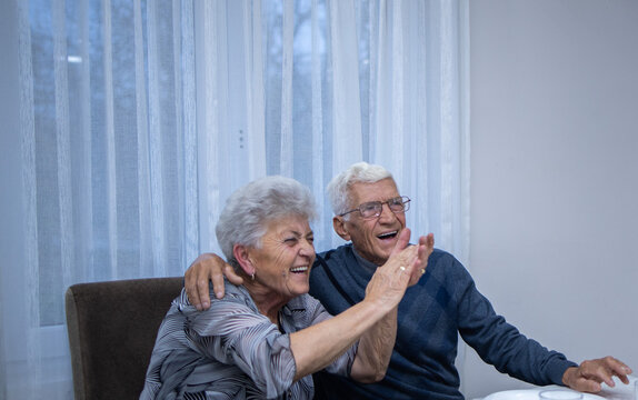 an elderly married couple in each other's arms is smiling proudly. a man is celebrating his 80th birthday, hugging his wife who is applauding and smiling. happy elderly couple. a family moment - Powered by Adobe