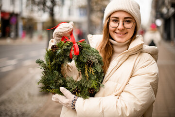 smiling woman holds circle wreath of twigs of thuja and spruce in her hands.