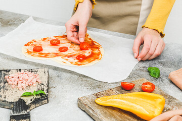 Obraz na płótnie Canvas Hands of caucasian teenage girl lay down sliced cherry tomato on heart-shaped pizza dough.