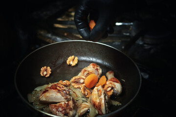 Chicken is cooked in a pan with nuts and dried apricots