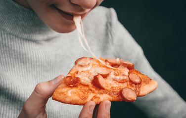 Happy caucasian girl holding a slice of pizza with stretching mozzarella cheese in her hand and biting .